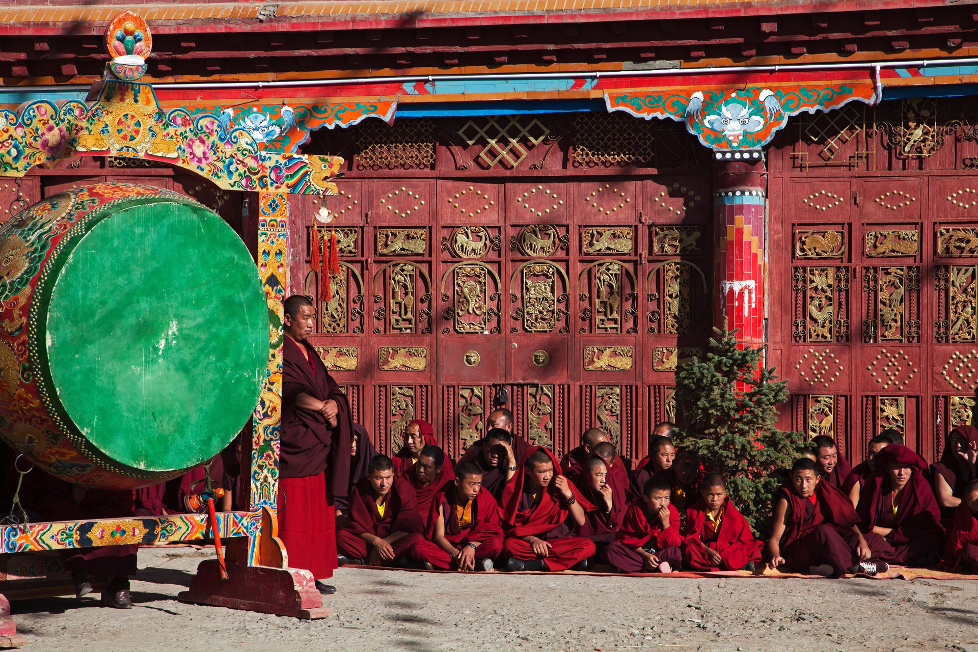 Tibetan monks in red robes beside a ceremonial prayer drum , reflecting Tibetan Buddhist spiritual heritage