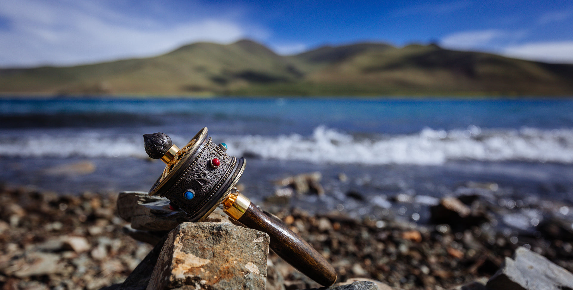 Tibetan prayer wheel resting on rocks beside a lake on the Tibetan Plateau